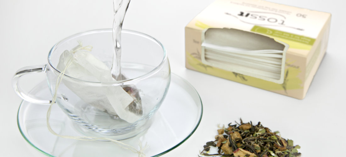 Tee wird in einer Tasse aus Glas aufgegossen, geöffnete Tossit Verpackung im Hintergrund